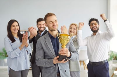 employee recognition. one employee holds a trophy while others cheer